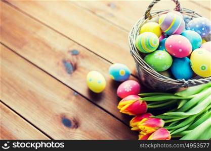 easter, holidays, tradition and object concept - close up of colored easter eggs in basket and tulip flowers on wooden table with copy space. close up of easter eggs in basket and flowers