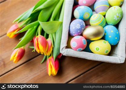 easter, holidays, tradition and object concept - close up of colored easter eggs in basket and tulip flowers