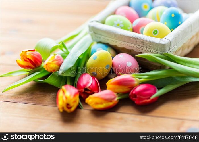 Easter, holidays, tradition and object concept - close up of colored easter eggs in basket and tulip flowers