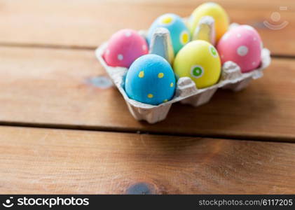 easter, holidays, tradition and object concept - close up of colored easter eggs in egg box or carton wooden surface