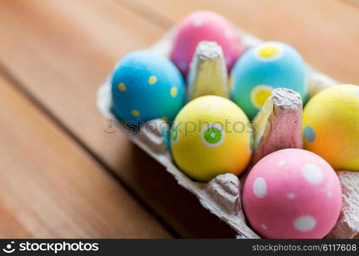 easter, holidays, tradition and object concept - close up of colored easter eggs in egg box or carton wooden surface