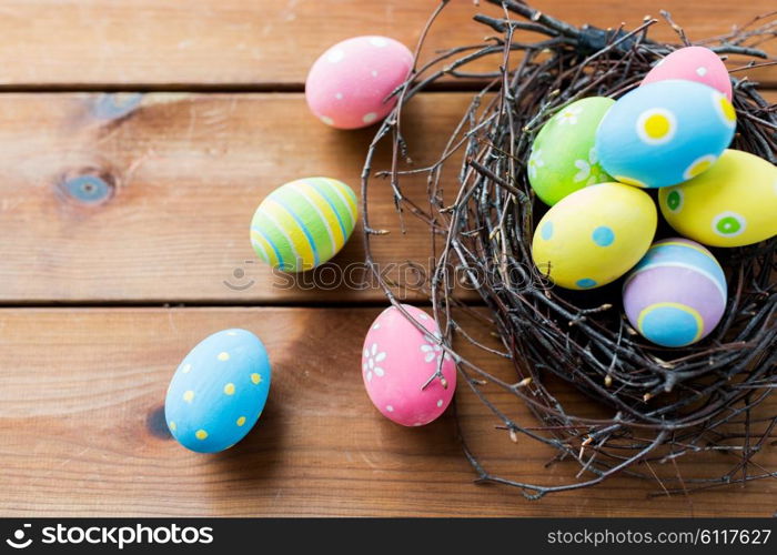 easter, holidays, tradition and object concept - close up of colored easter eggs in nest on wooden surface