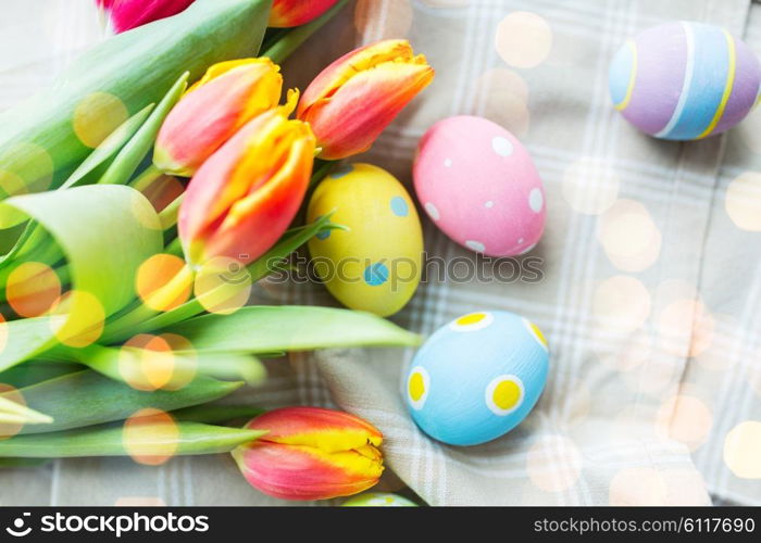 easter, holidays, tradition and object concept - close up of colored easter eggs in basket and tulip flowers