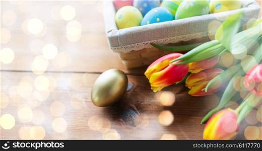 easter, holidays, tradition and object concept - close up of colored easter eggs in basket and tulip flowers