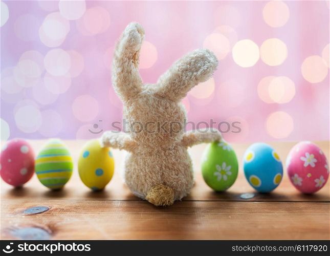 easter, holidays, tradition and object concept - close up of colored easter eggs and bunny over pink holidays lights background