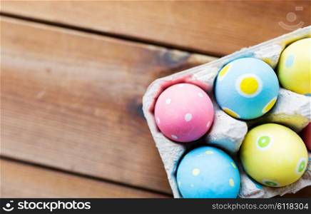 easter, holidays, tradition and object concept - close up of colored easter eggs in egg box or carton wooden surface with copy space