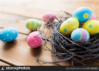 easter, holidays, tradition and object concept - close up of colored easter eggs in nest on wooden surface