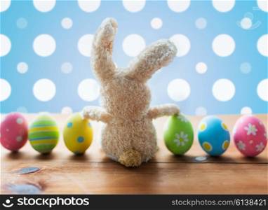 easter, holidays, tradition and object concept - close up of colored easter eggs and bunny over blue polka dot background