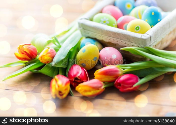 Easter, holidays, tradition and object concept - close up of colored easter eggs in basket and tulip flowers