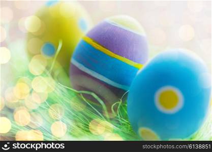 easter, holidays, tradition and object concept - close up of colored easter eggs and decorative grass on wooden surface over holidays lights