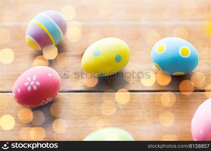 easter, holidays, tradition and object concept - close up of colored easter eggs on wooden surface over holidays lights