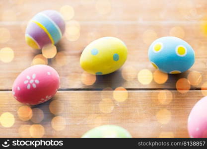 easter, holidays, tradition and object concept - close up of colored easter eggs on wooden surface over holidays lights