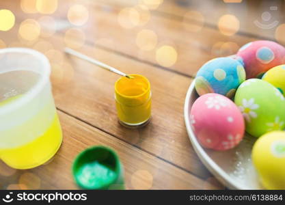 easter, holidays, tradition and object concept - close up of colored easter eggs on plate over holidays lights