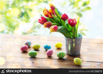 easter, holidays, tradition and object concept - close up of colored easter eggs and tulip flowers in tin bucket on wooden table over green natural background