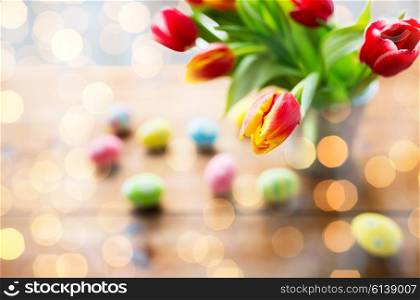 easter, holidays, tradition and object concept - close up of colored easter eggs and tulip flowers in bucket on wooden table
