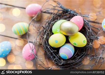 easter, holidays, tradition and object concept - close up of colored easter eggs in nest on wooden surface over lights