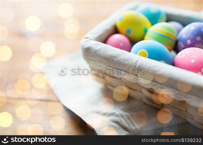 easter, holidays, tradition and object concept - close up of colored easter eggs in wicker basket over lights