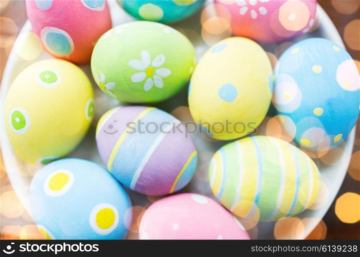 easter, holidays, tradition and object concept - close up of colored easter eggs on plate over lights
