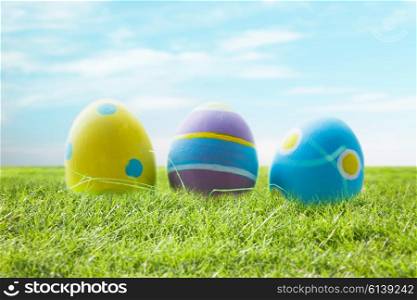easter, holidays, tradition and object concept - close up of colored easter eggs and decorative grass on wooden surface over blue sky and grass background