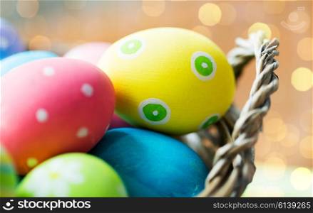 easter, holidays, tradition and object concept - close up of colored easter eggs in basket over holidays lights