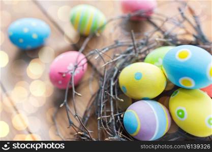 easter, holidays, tradition and object concept - close up of colored easter eggs in nest on wooden surface over lights