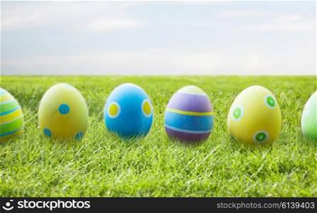 easter, holidays, tradition and object concept - close up of colored easter eggs on wooden surface over blue sky and grass background