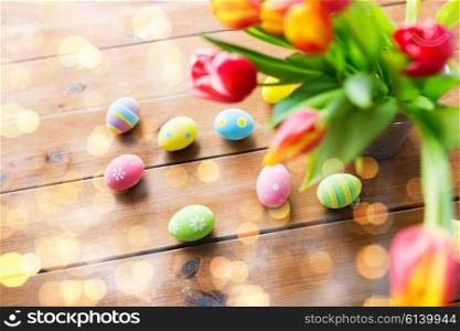 easter, holidays, tradition and object concept - close up of colored easter eggs and tulip flowers in bucket on wooden table over holidays lights
