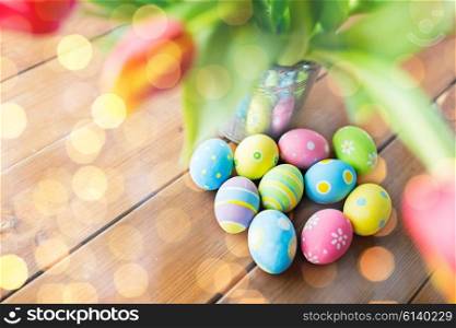 easter, holidays, tradition and object concept - close up of colored easter eggs and tulip flowers in bucket on wooden table over lights