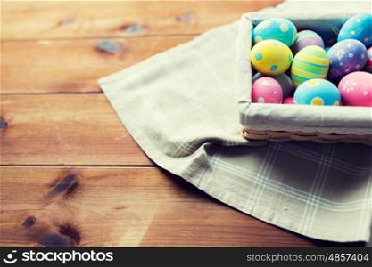 easter, holidays, tradition and object concept - close up of colored easter eggs in wicker basket