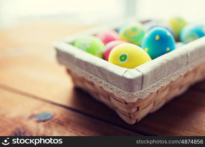 easter, holidays, tradition and object concept - close up of colored easter eggs in wicker basket