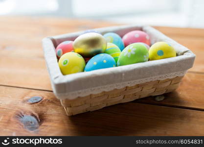 easter, holidays, tradition and object concept - close up of colored easter eggs in wicker basket