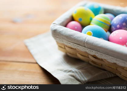 easter, holidays, tradition and object concept - close up of colored easter eggs in wicker basket