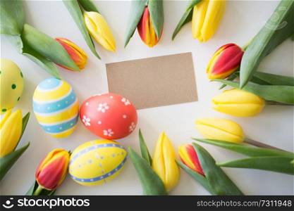 easter, holidays, tradition and object concept - close up of colored eggs and tulip flowers on white background. close up of colored easter eggs and tulip flowers