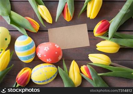 easter, holidays, tradition and object concept - close up of colored eggs and tulip flowers over wooden boards background. close up of colored easter eggs and tulip flowers