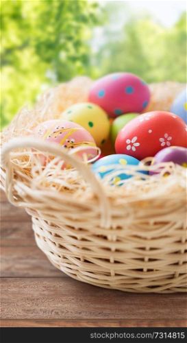 easter, holidays, tradition and object concept - close up of colored eggs in basket on wooden table over green natural background. close up of colored easter eggs in basket
