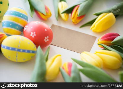 easter, holidays, tradition and object concept - close up of colored eggs and tulip flowers on white background. close up of colored easter eggs and tulip flowers