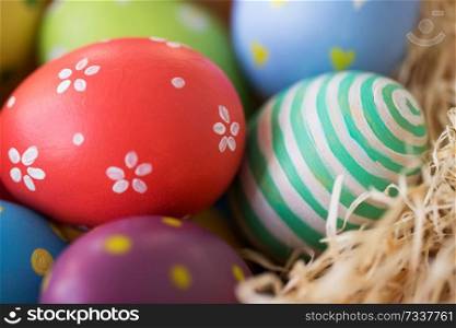 easter, holidays, tradition and object concept - close up of colored eggs in straw. close up of colored easter eggs in straw