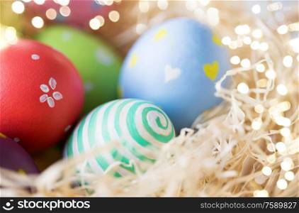 easter, holidays, tradition and object concept - close up of colored eggs in straw. close up of colored easter eggs in straw