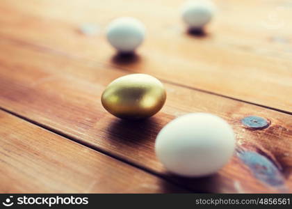 easter, holidays, tradition and object concept - close up of golden and white easter eggs on wood