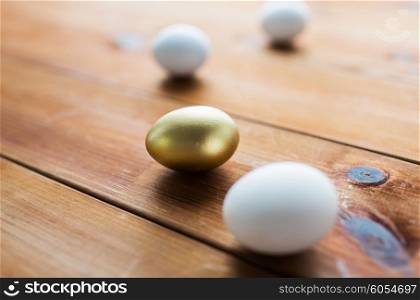 easter, holidays, tradition and object concept - close up of golden and white easter eggs on wood