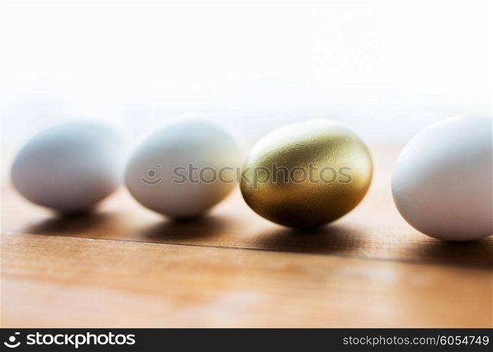 easter, holidays, tradition and object concept - close up of golden and white easter eggs on wood
