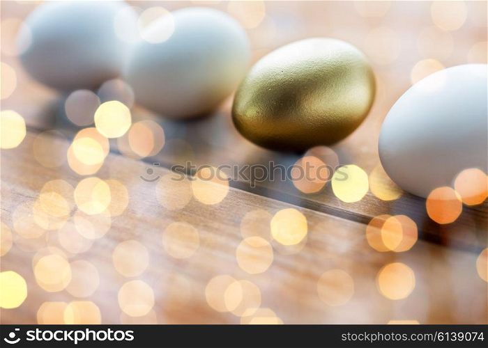 easter, holidays, tradition and object concept - close up of golden and white easter eggs on wood over lights