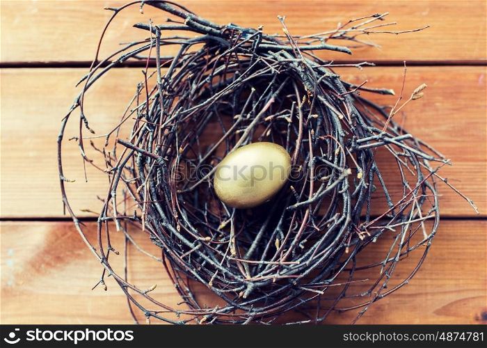 easter, holidays, tradition and object concept - close up of golden easter egg in nest on wooden surface