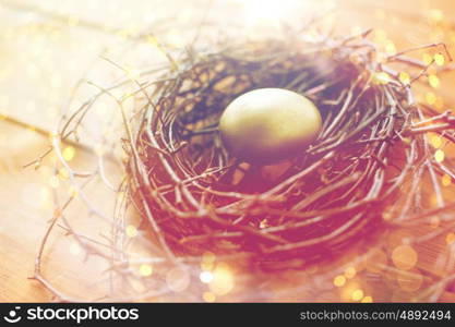 easter, holidays, tradition and object concept - close up of golden easter egg in nest on wooden surface