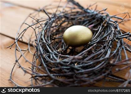 easter, holidays, tradition and object concept - close up of golden easter egg in nest on wooden surface