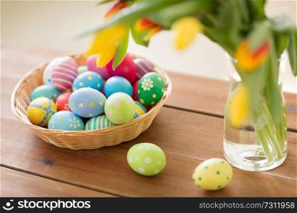 easter, holidays, tradition and object concept - colored eggs in basket and tulip flowers at home. colored easter eggs in basket and flowers at home