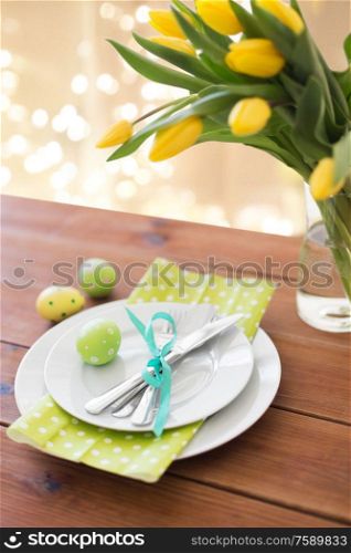 easter, holidays, tradition and object concept - green colored egg, plates with cutlery and tulip flowers on table at home. easter egg, plates, cutlery and tulip flowers