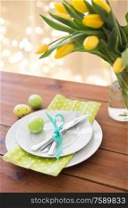 easter, holidays, tradition and object concept - green colored egg, plates with cutlery and tulip flowers on table at home. easter egg, plates, cutlery and tulip flowers