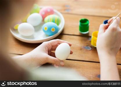 easter, holidays, tradition and people concept - close up of woman coloring easter eggs with colors and brush