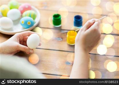 easter, holidays, tradition and people concept - close up of woman coloring easter eggs with colors and brush